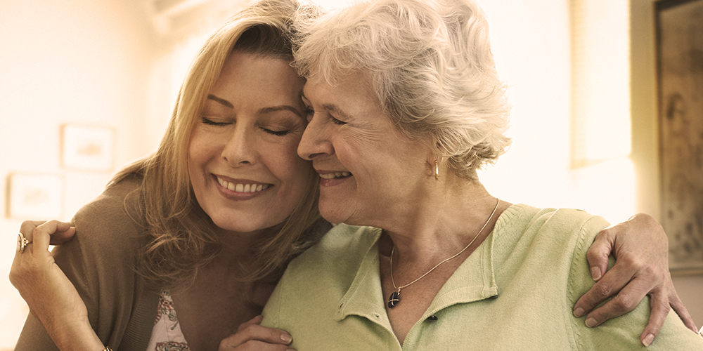 Younger woman and an older woman smiling in embrace  Younger woman and an older woman smiling in embrace